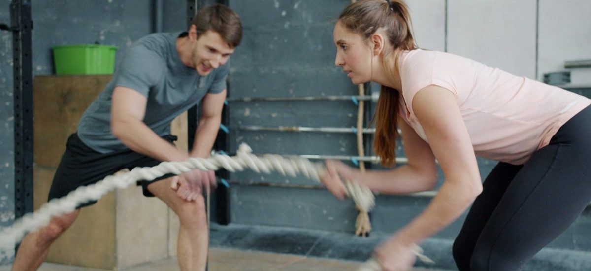 Portrait of young attractive sportswoman exercising with battle ropes in gym with support of sports trainer handsome guy in sportswear. People and sports concept.