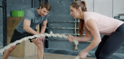 Portrait of young attractive sportswoman exercising with battle ropes in gym with support of sports trainer handsome guy in sportswear. People and sports concept.