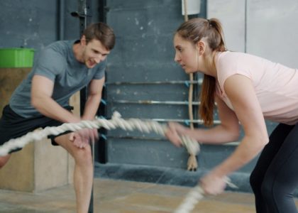 Portrait of young attractive sportswoman exercising with battle ropes in gym with support of sports trainer handsome guy in sportswear. People and sports concept.